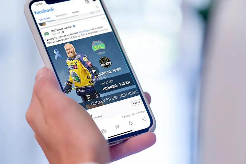 En person som blar gjennom en Storhamar Hockey-annonse for et spill på smarttelefonen sin, med en illustrert målvakt og billettinformasjon.