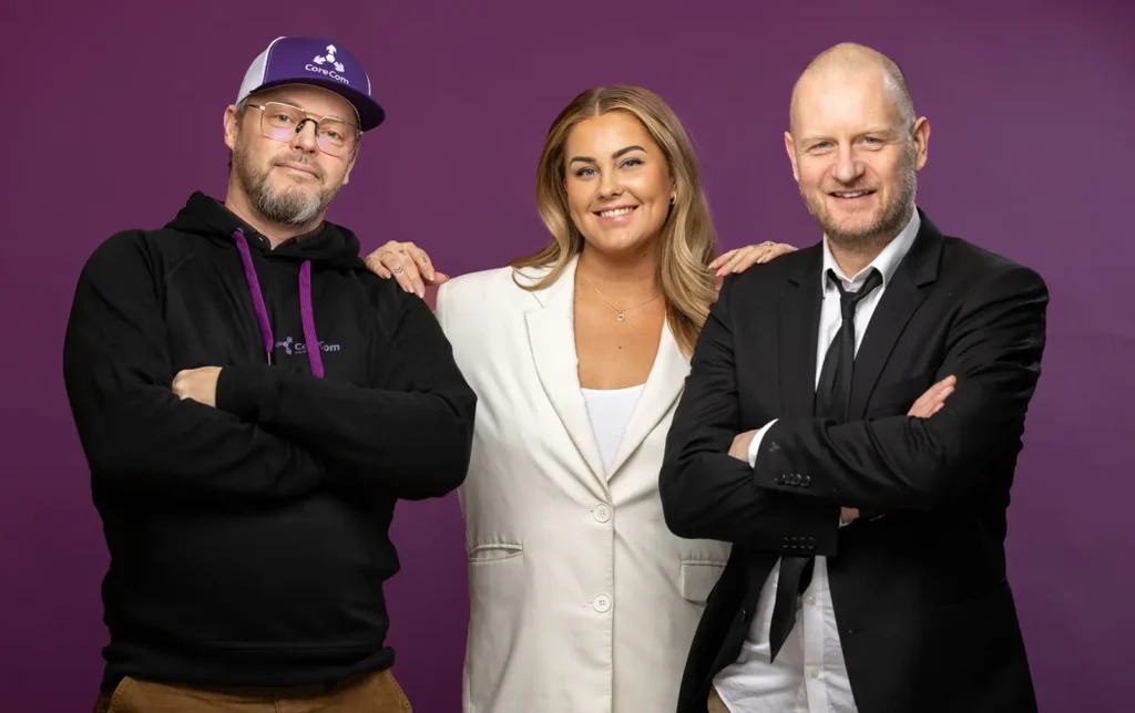 Tre individer, inkludert Victoria Moen Toth, står på rekke og rad mot en lilla bakgrunn, hver smilende. Personen til venstre har på seg baseballcaps og hettegenser, mellompersonen er i en hvit blazer, og den til høyre er i dress.