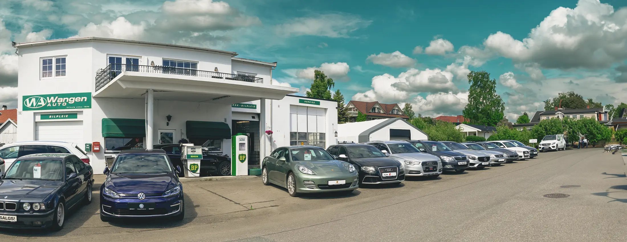 En rad med biler står parkert utenfor Wangen Autos servicesenter, en hvit bygning med grønn skilting, som fremhever deres digitale heis for forbedret kundeservice gjennom den nye nettsiden.