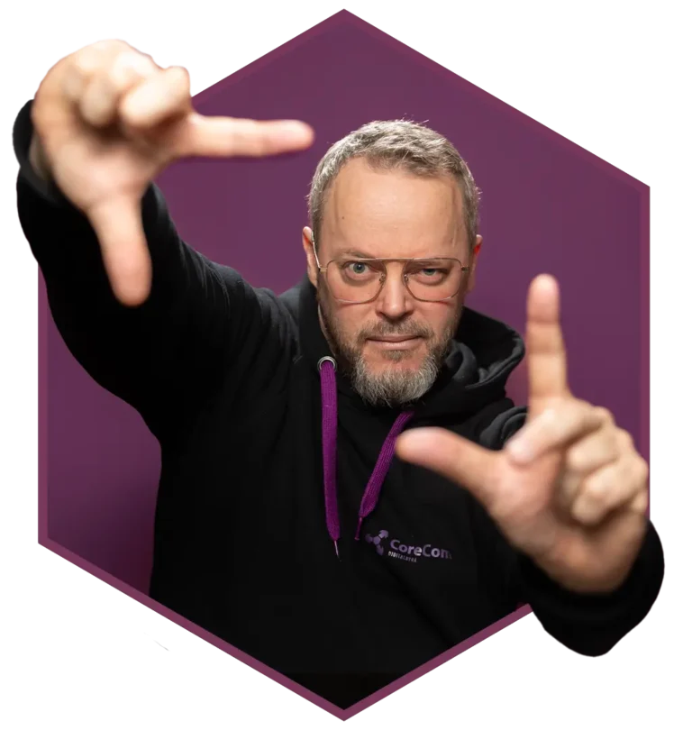 En mann i briller og mørk hettegenser, som minner om en nettsidedesigner, rammer inn ansiktet med hendene mot en lilla bakgrunn.