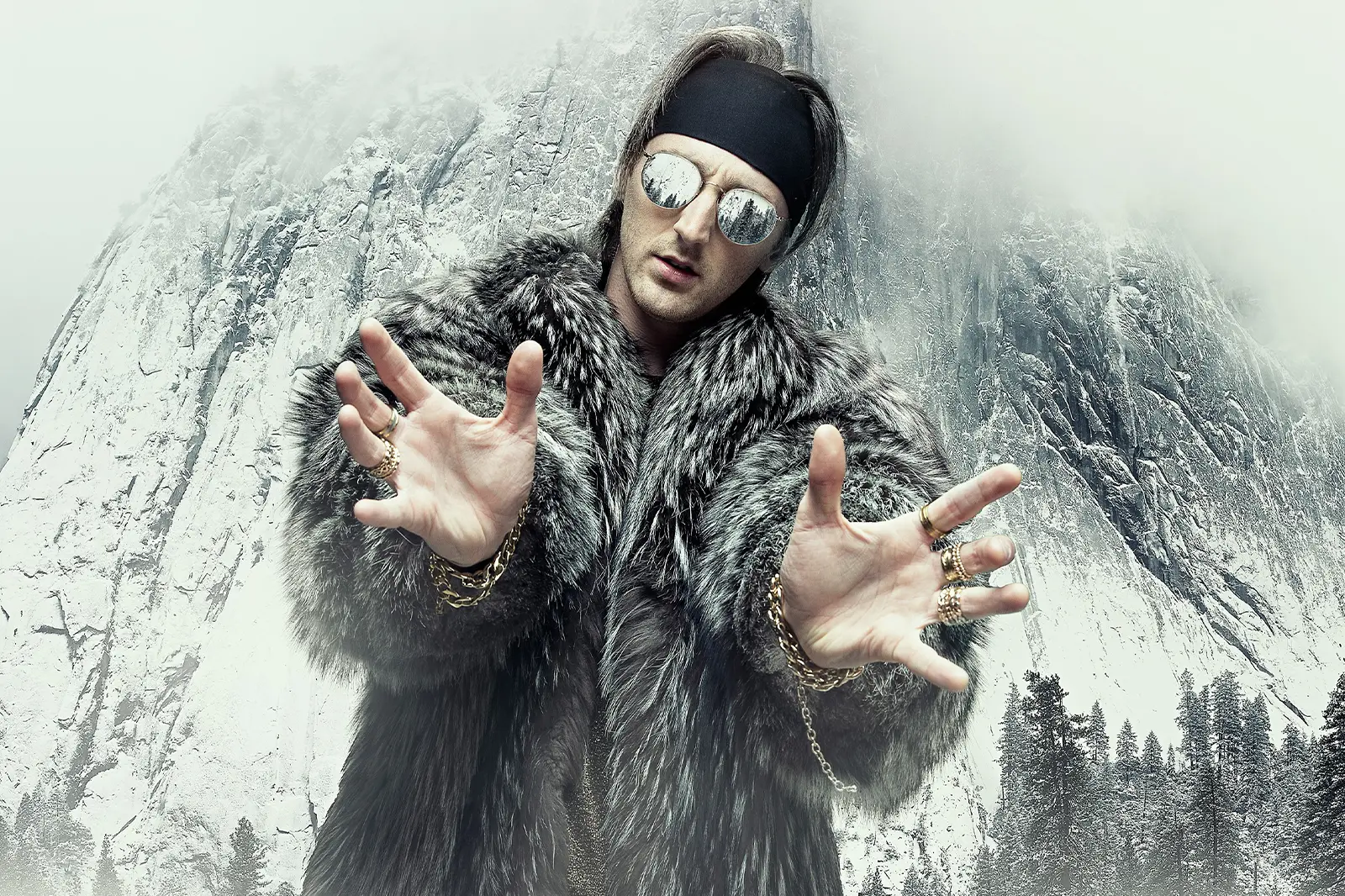 Anders Viken, iført pelsfrakk, solbriller og pannebånd, poserer med hendene utstrakt foran et snødekt fjell i bakgrunnen.