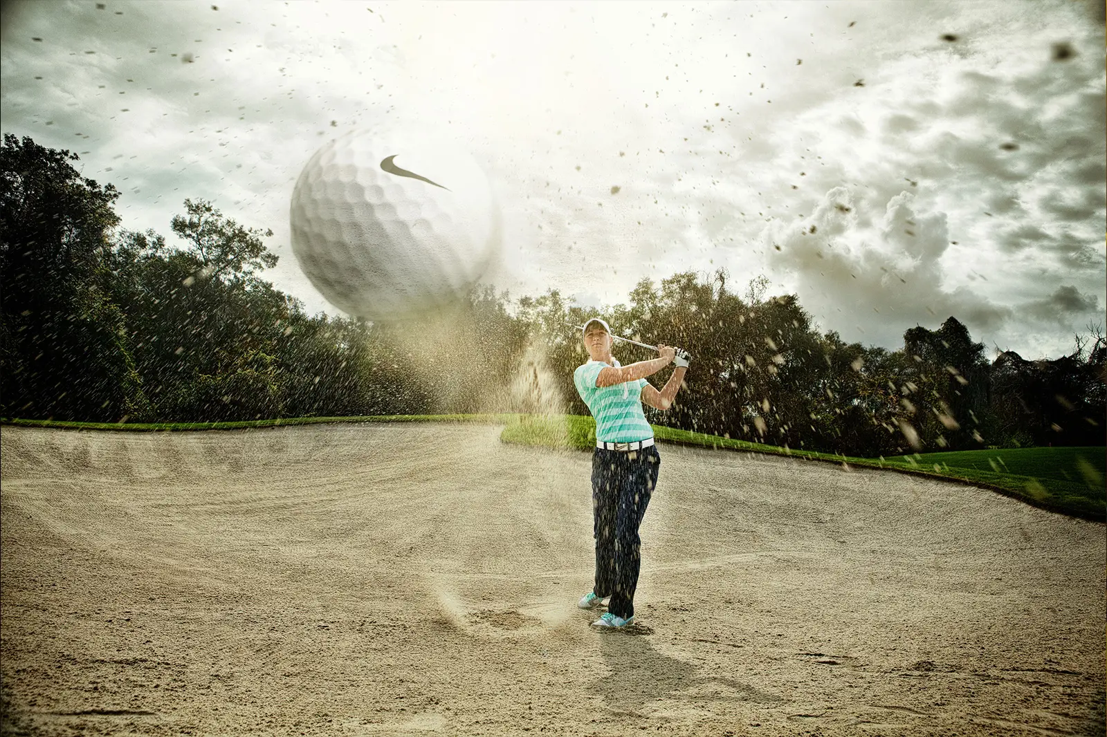 Anders Viken slår et slag fra en sandbunker, med sand som flyr og en stor golfball som dukker opp nær kameraet under en overskyet himmel.