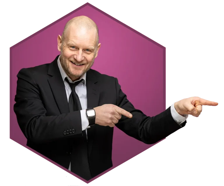 En skallet mann i svart dress og slips smiler og peker til høyre, står foran en lilla sekskantet bakgrunn, noe som antyder suksess innen digital markedsføring.